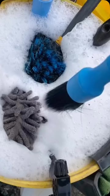 Detailing brushes and wash mitts in a bucket of soap foam