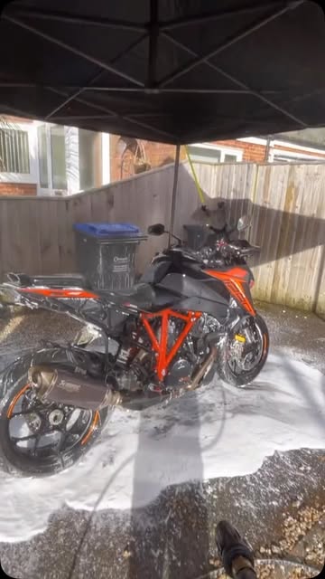 Orange and black motorcycle rinsed after a foam wash under a canopy