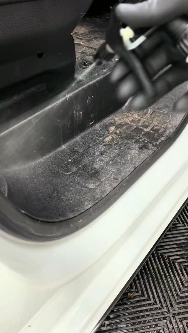 Gloved hand spraying a dirty black door sill and floor liner